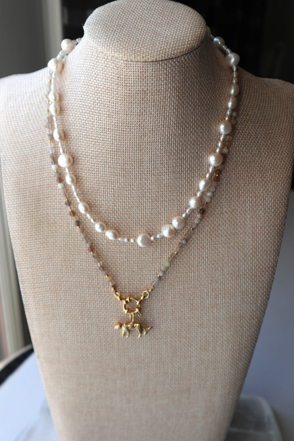 Marula necklace by Auréad Designs displayed on a linen bust form, layered with a freshwater pearl necklace, with the gold stainless steel leopard charm as the focal point of the stack