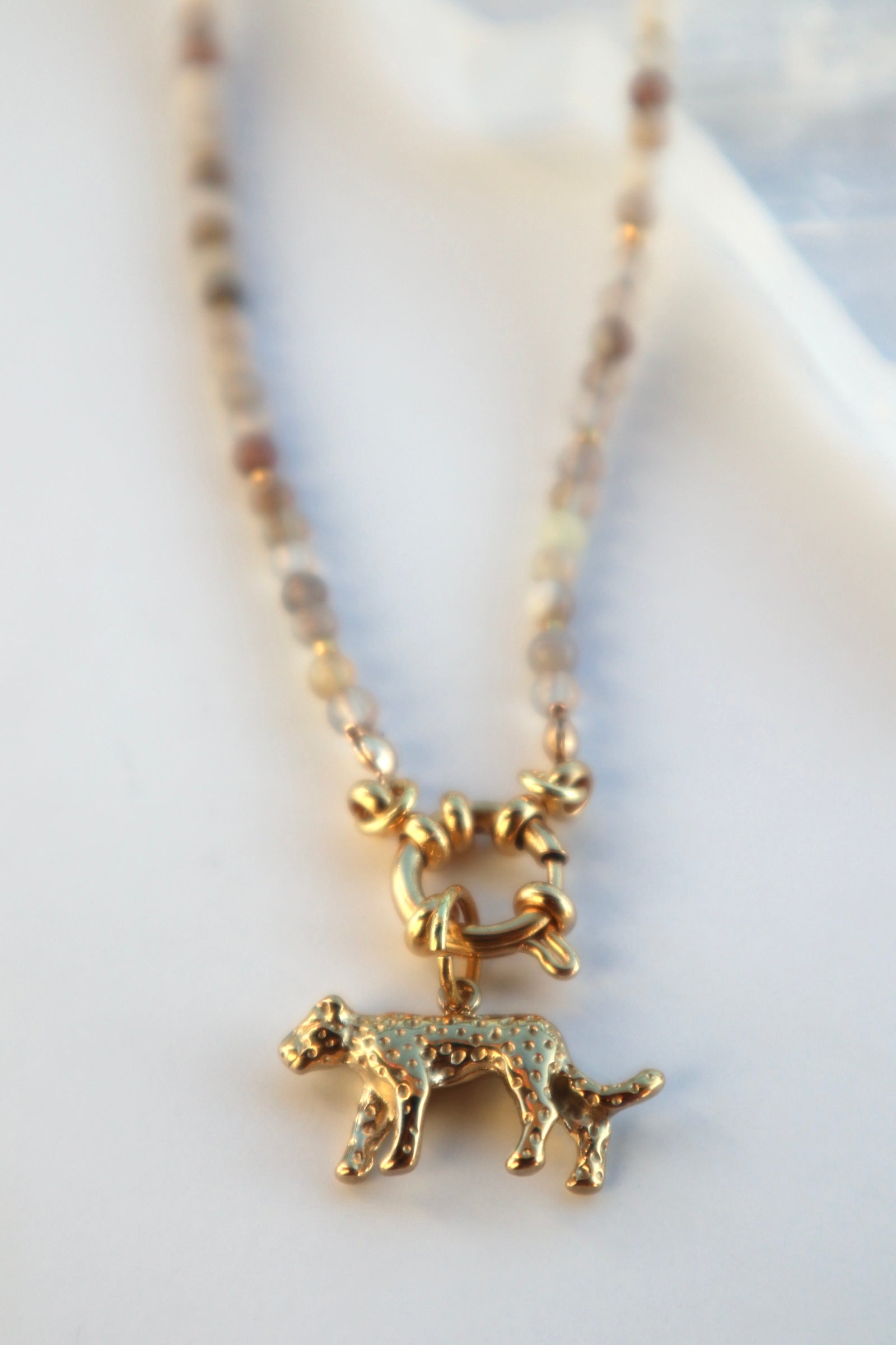 Macro detail of the Marula necklace highlighting the sculptural gold stainless steel leopard charm and the natural banding of Botswana agate beads