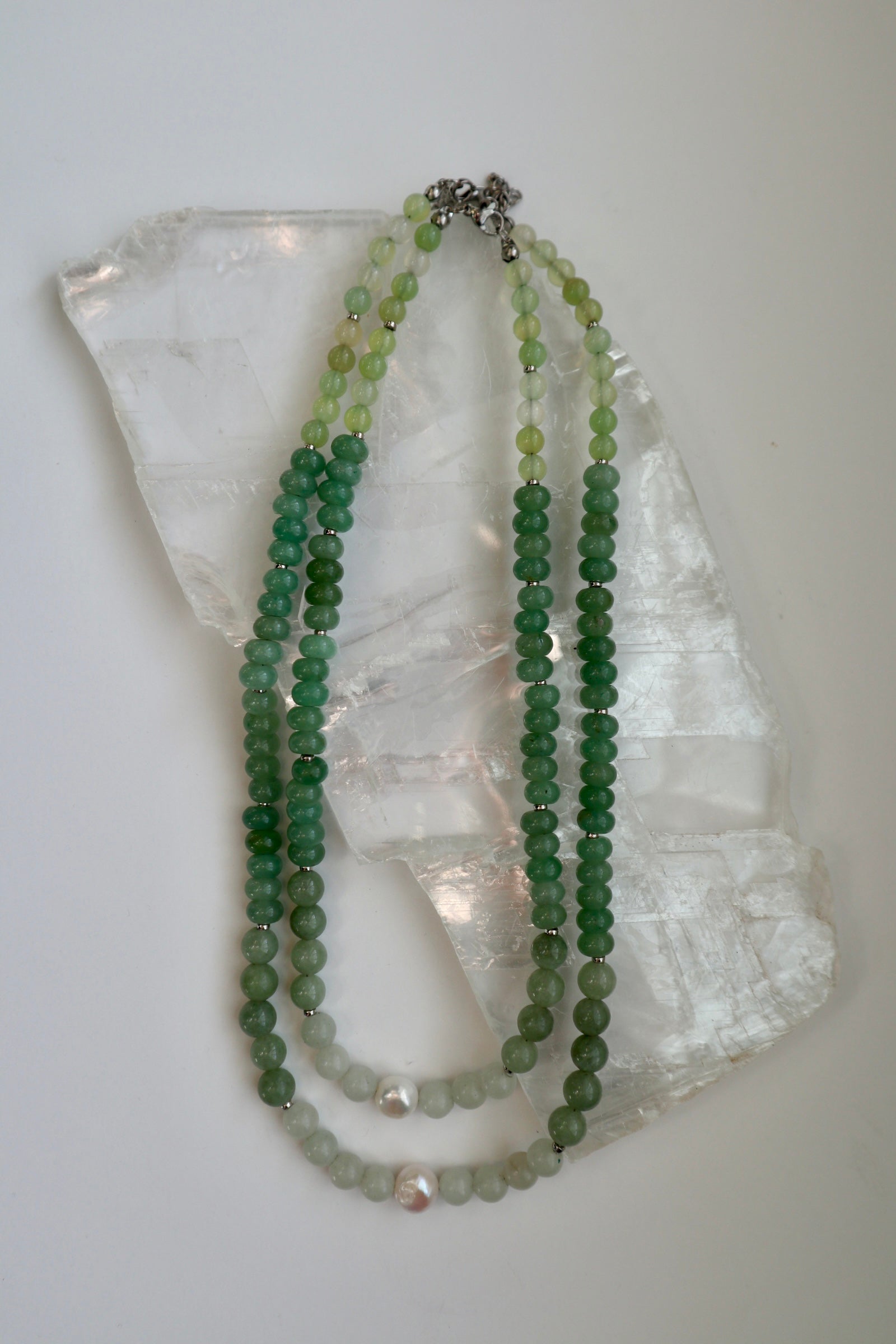 Meadowe necklace by Auréad Designs in both available lengths draped on a white selenite slab, showing the natural gradient of green jade beads and the freshwater pearl accent