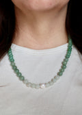 Close-up of the Meadowe necklace resting at the collarbone, highlighting the soft green and lavender tones of jade and grape agate beads with the luminous freshwater pearl against skin
