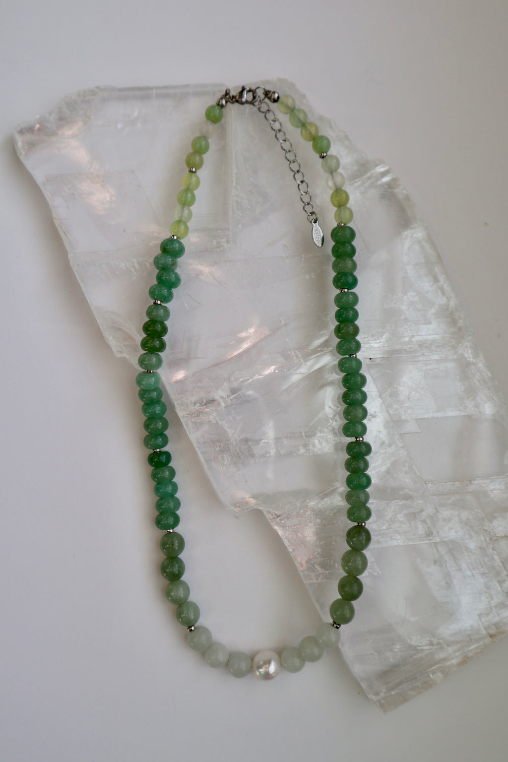 Meadowe necklace by Auréad Designs, featuring green jade beads, grape agate beads, and a freshwater pearl accent with a stainless steel clasp, laid flat on a white selenite slab