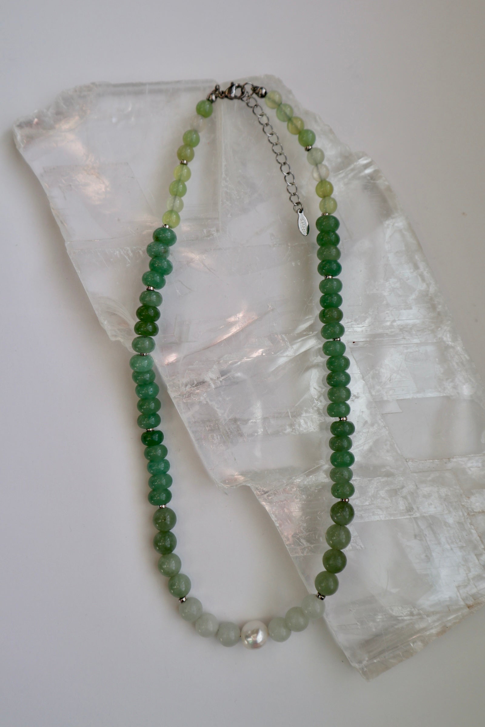 Meadowe necklace by Auréad Designs, featuring green jade beads, grape agate beads, and a freshwater pearl accent with a stainless steel clasp, laid flat on a white selenite slab