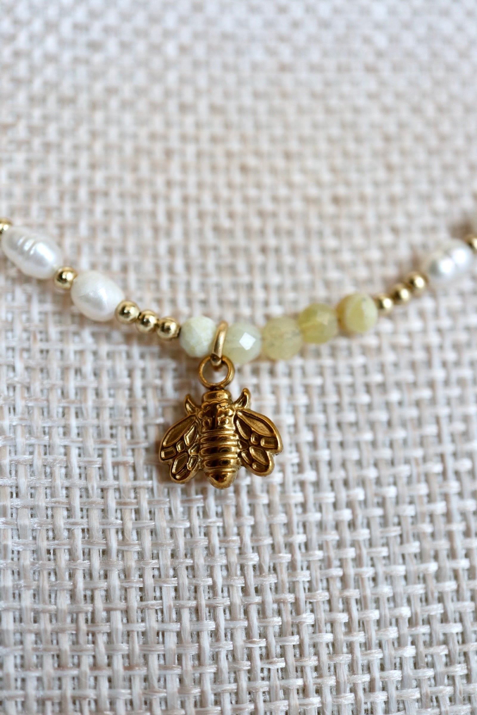Auréad Designs Melline necklace close-up of gold IP stainless steel bee charm dangling at center, flanked by yellow opal beads, freshwater rice pearls, and gold micro spacer beads on linen bust form