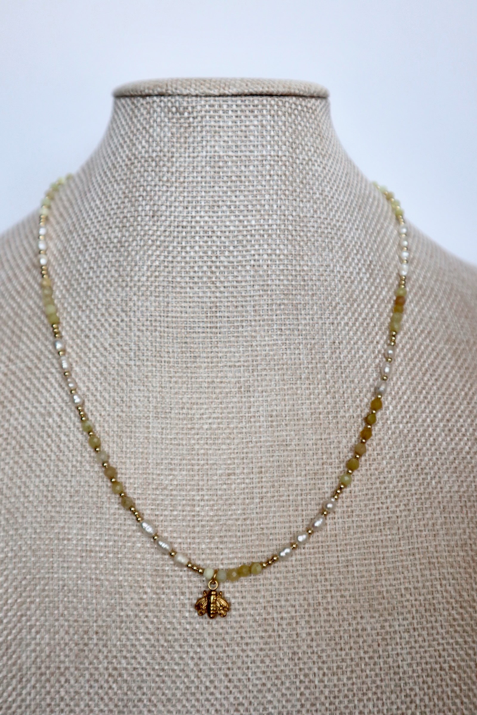 Auréad Designs Melline necklace displayed front-facing on linen bust form, full strand of yellow opal beads, freshwater rice pearls, and gold spacers with bee charm centered at front
