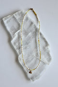 Auréad Designs Melline necklace laid flat on white selenite slab, showing full strand of yellow opal beads, freshwater rice pearls, gold micro spacer beads, and gold bee charm with lobster clasp