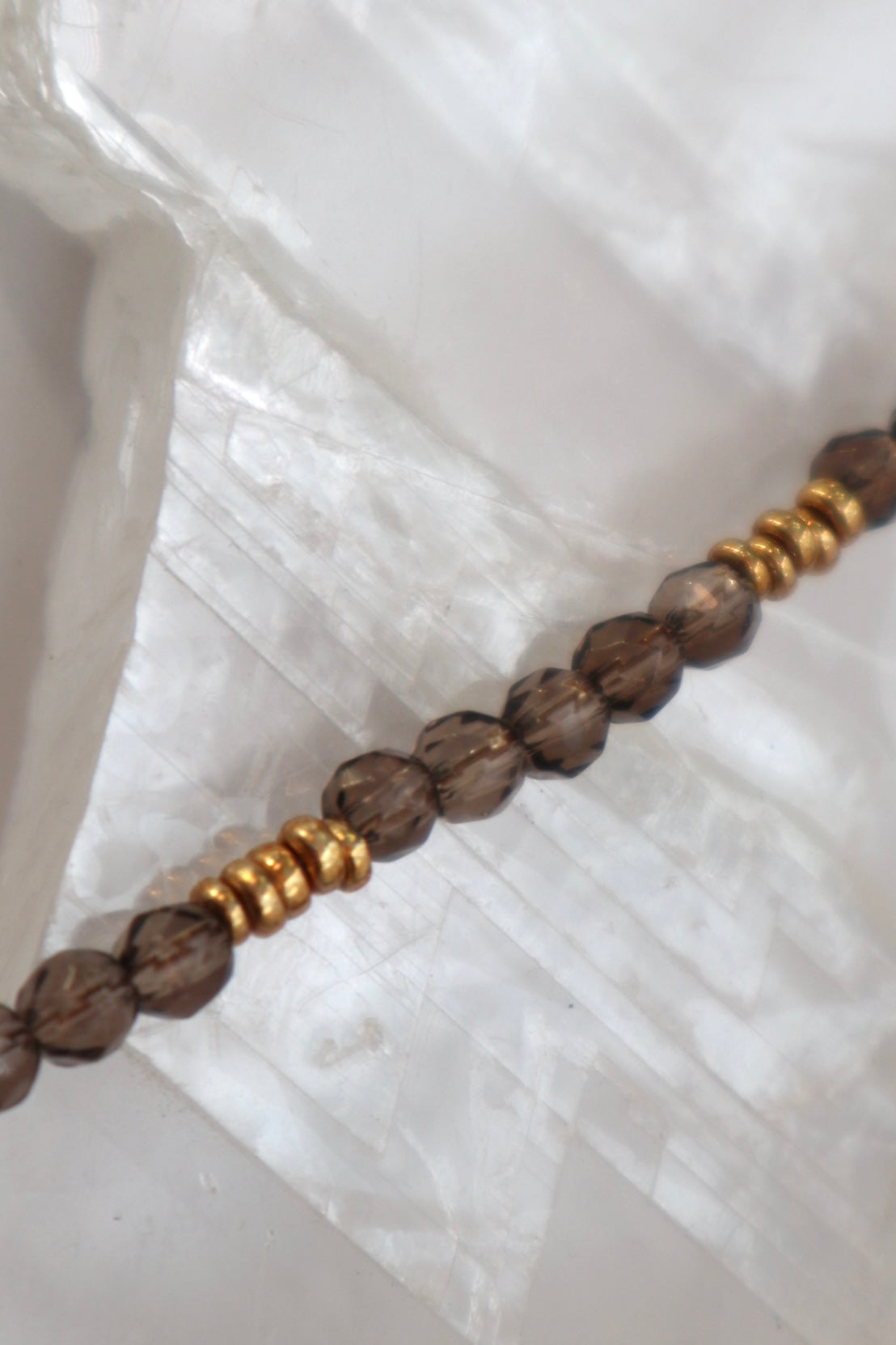 Close-up of the Mira necklace on a white selenite slab, highlighting the translucent deep brown tones of smoky quartz beads alongside galvanized gold spacer beads