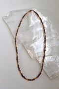 Mira necklace by Auréad Designs, featuring smoky quartz gemstone beads and galvanized gold spacer beads with a 14k gold-filled clasp, laid flat on a white selenite slab