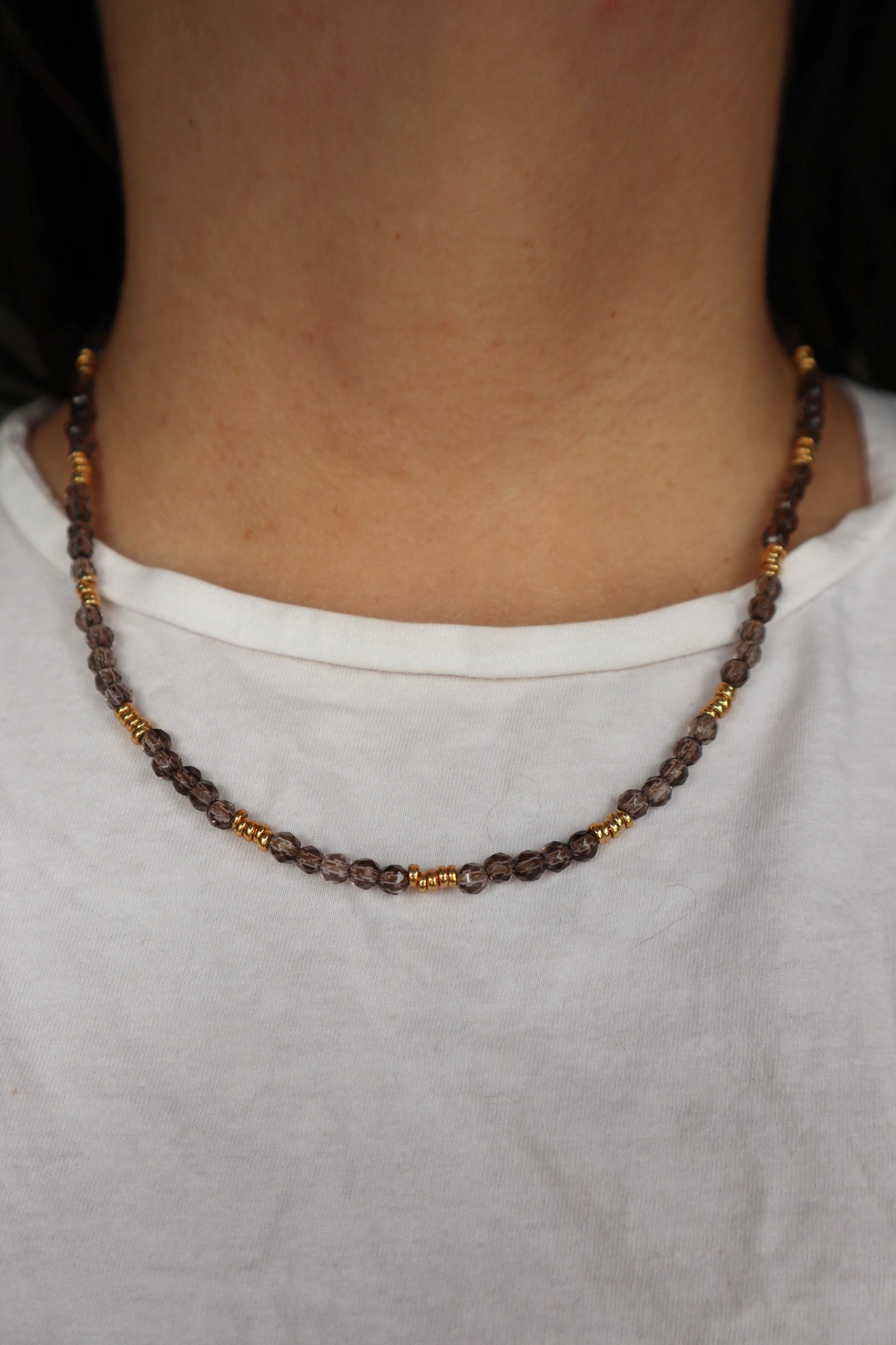 Mira smoky quartz necklace worn at the collarbone, showing the deep translucent brown tones of the smoky quartz beads and warm gold spacer accents against skin