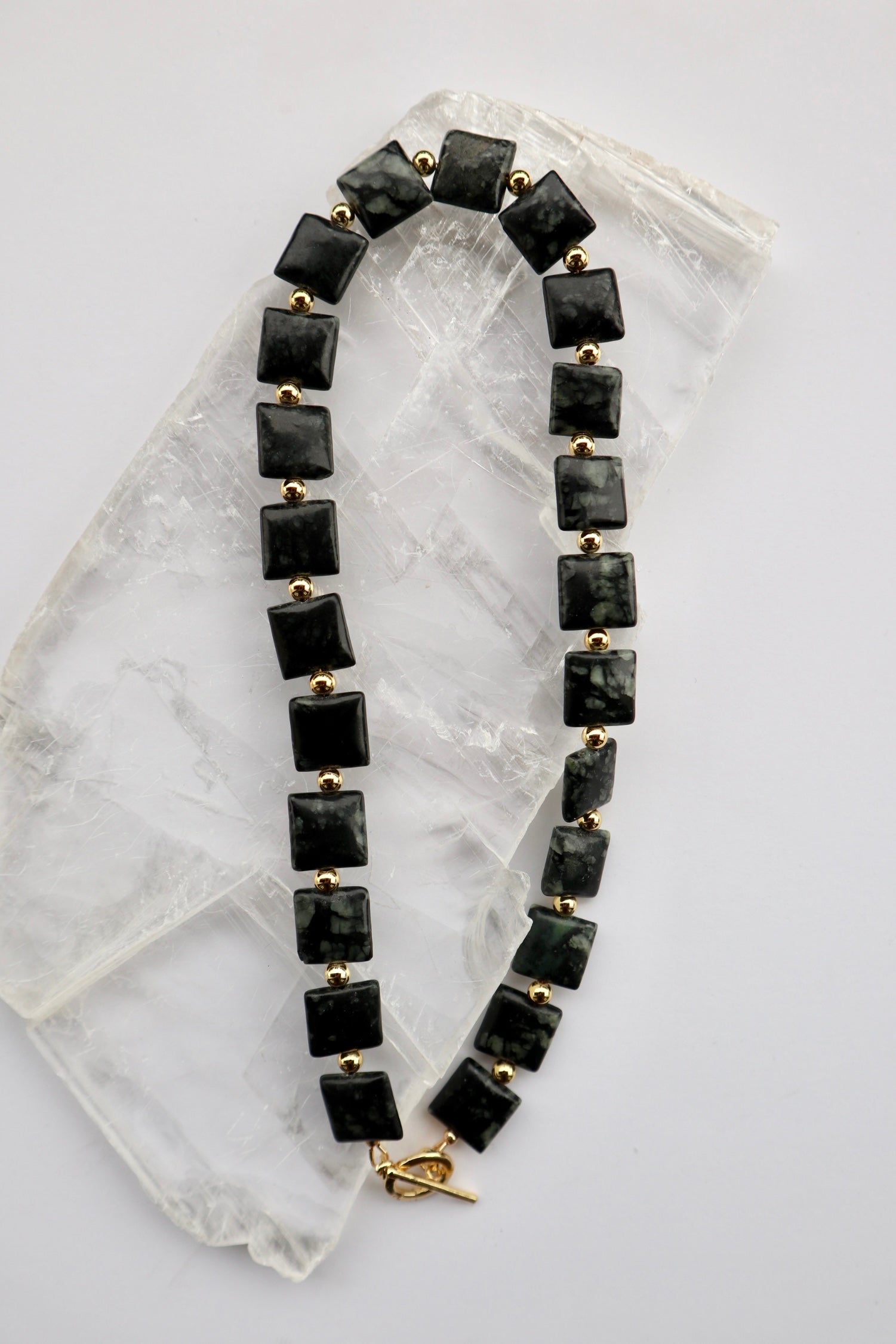 Morenne necklace by Auréad Designs, featuring Picasso serpentine pillow beads and gold-filled round spacer beads with a gold-filled toggle clasp, laid flat on a white selenite slab