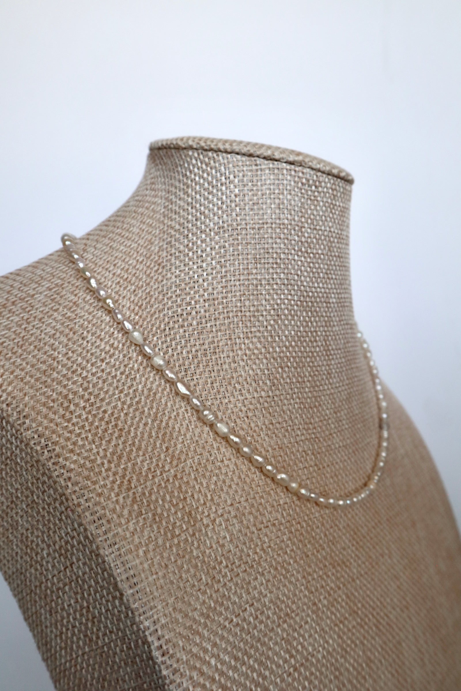 Auréad Designs Nacrine freshwater rice pearl necklace draped at an angle on linen bust form, showing full strand length at 16 inches