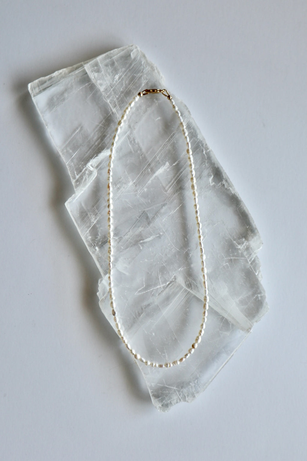 Auréad Designs Nacrine 16-inch freshwater rice pearl necklace with 14k gold-filled lobster clasp laid flat on white selenite slab