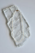 Auréad Designs Nacrine 16-inch freshwater rice pearl necklace with 14k gold-filled lobster clasp laid flat on white selenite slab