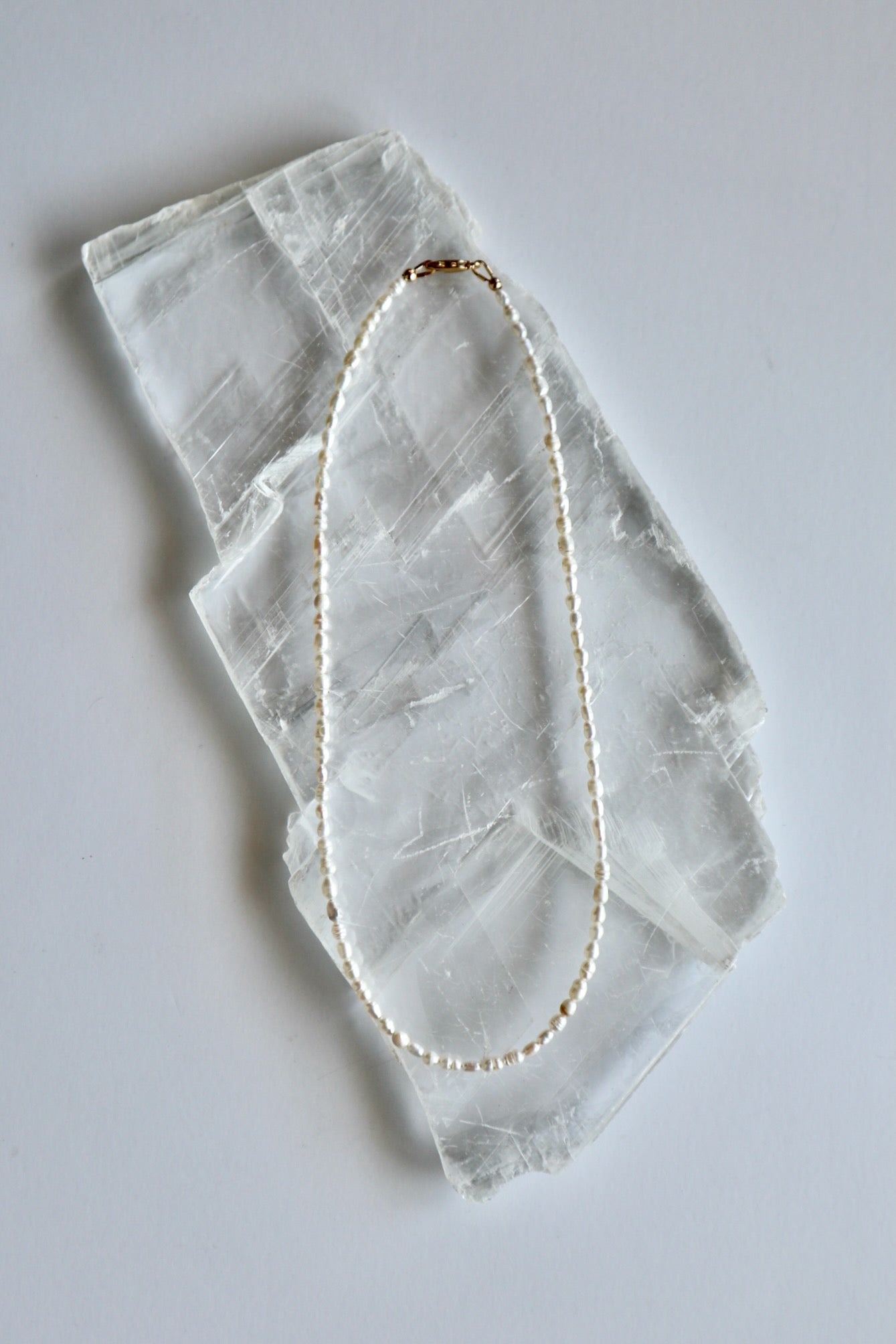 Auréad Designs Nacrine 16-inch freshwater rice pearl necklace with 14k gold-filled lobster clasp laid flat on white selenite slab