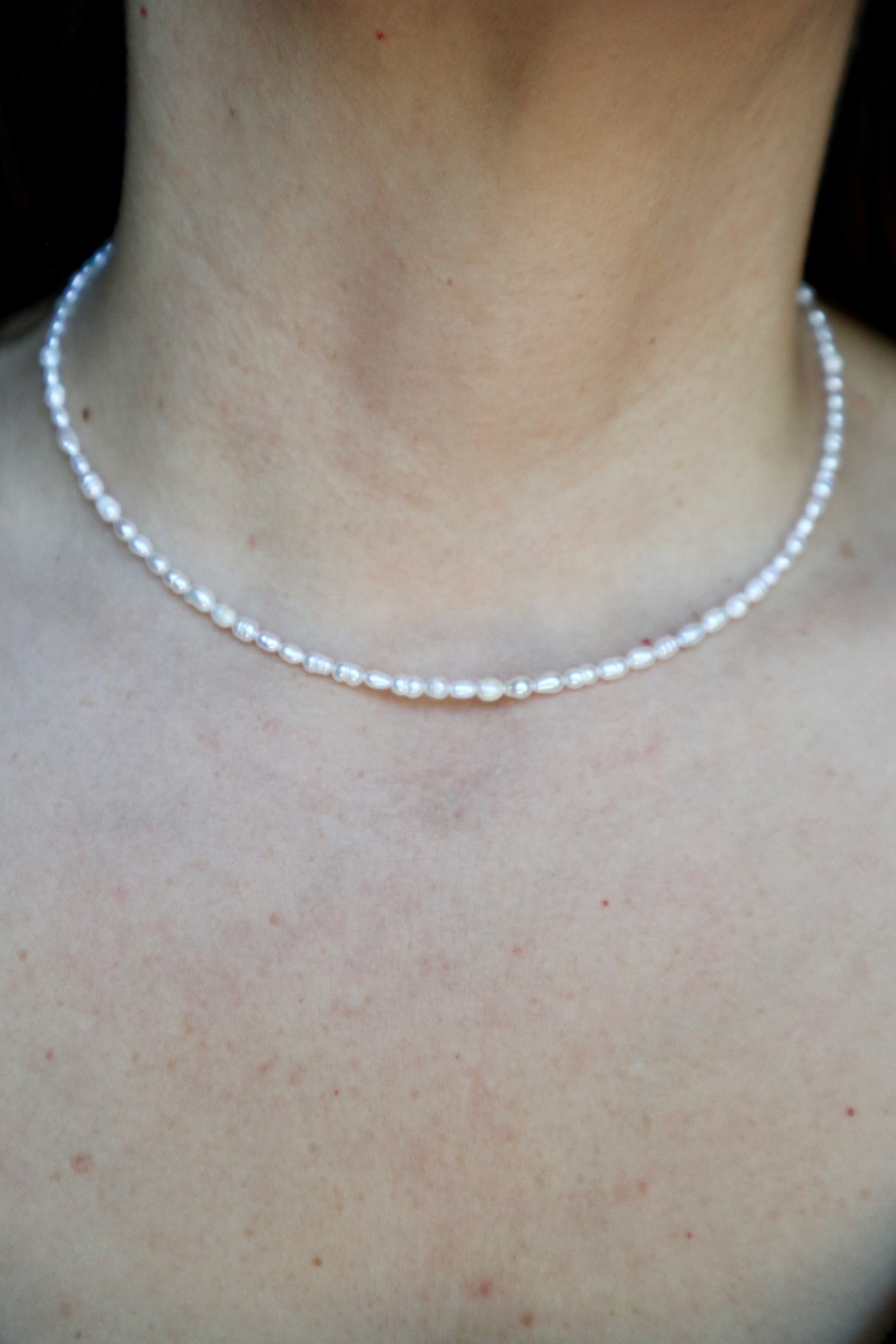 Auréad Designs Nacrine necklace worn at collarbone length against bare skin, showing the full continuous strand of grade 5A freshwater rice pearls sitting close to the neck against a dark background