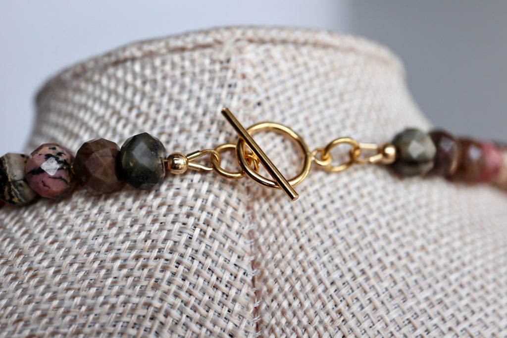 Close-up of the Noirrose necklace on a linen bust form, highlighting the 14k gold-filled toggle clasp and the natural deep rose and black veining of the faceted rhodonite rondelle beads