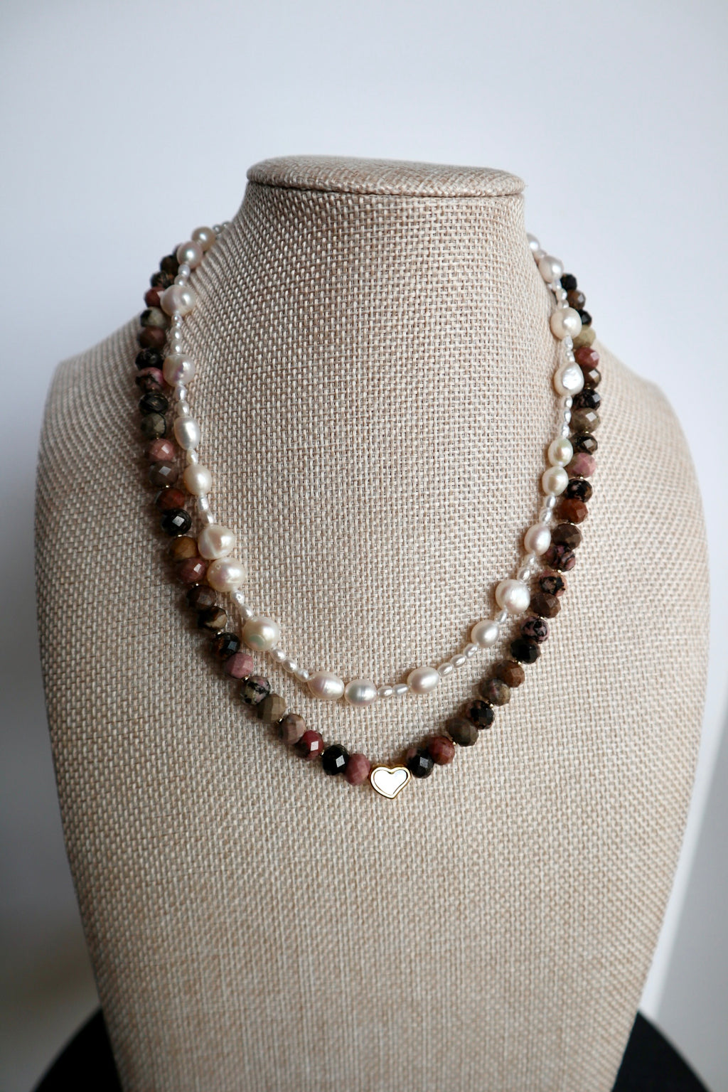 Noirrose necklace by Auréad Designs displayed on a linen bust form, showing the full strand of faceted rhodonite rondelle beads and gold heart charm with iridescent inlay