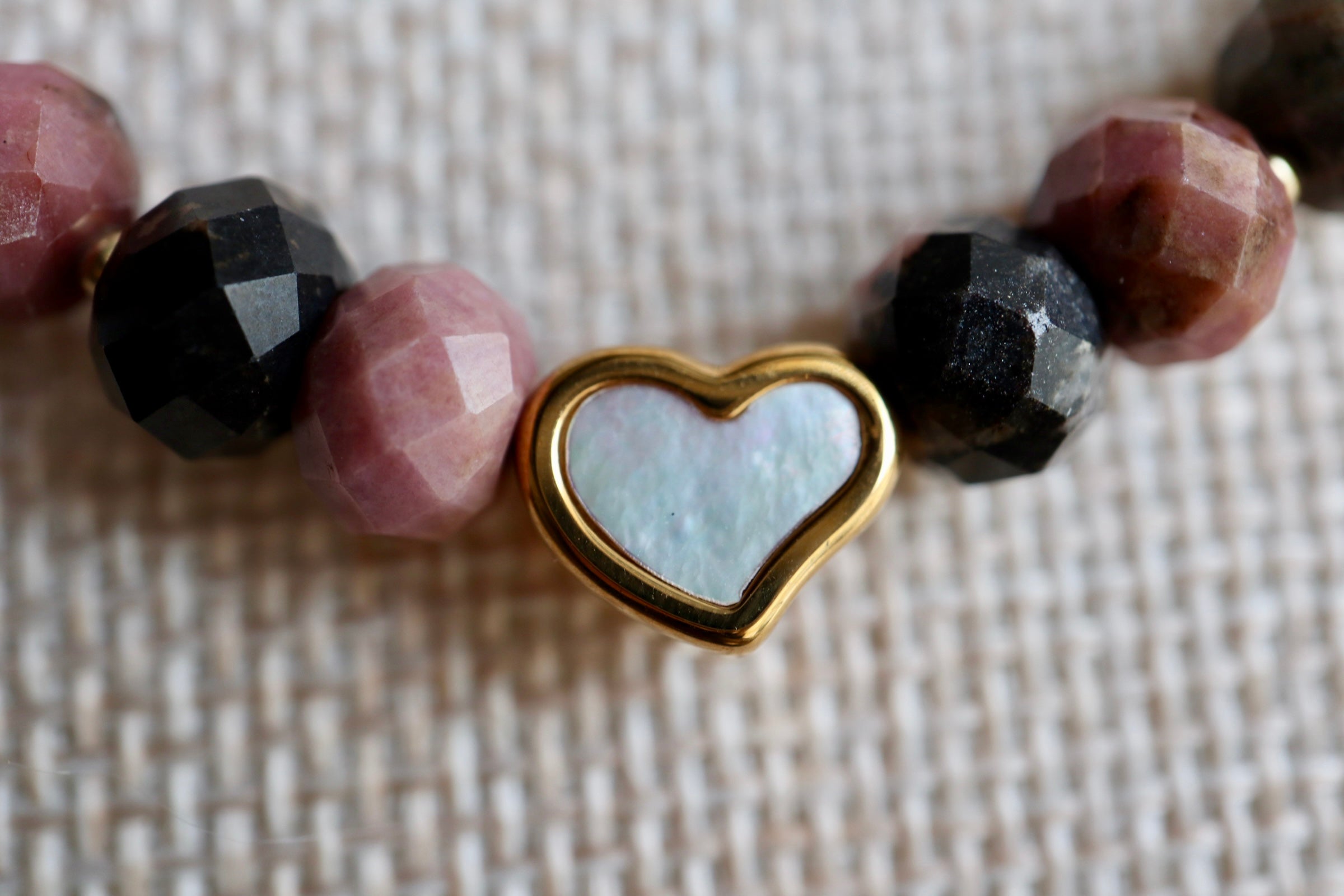 Detail shot of the Noirrose necklace highlighting the gold stainless steel heart charm with iridescent inlay and the 14k gold-filled toggle clasp against faceted rhodonite beads