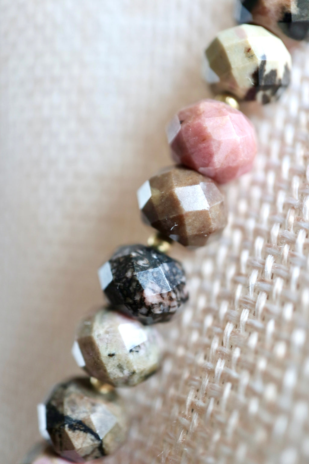 Close-up of the Noirrose necklace showing the deep rose tones and natural black veining of faceted rhodonite rondelle beads alongside the gold iridescent heart charm