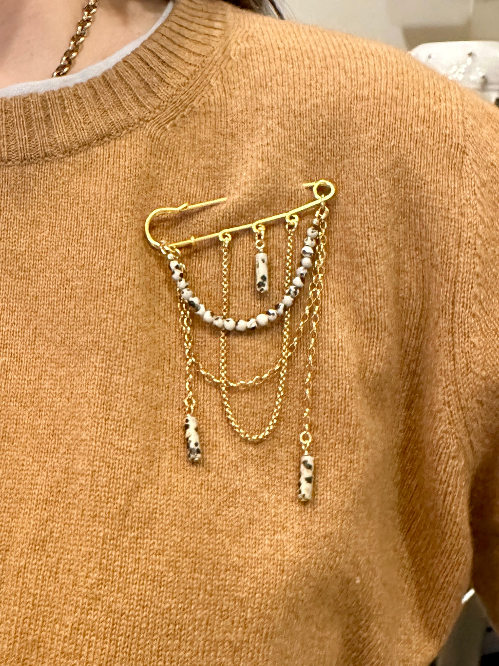 Perrin pin brooch by Auréad Designs worn on a cashmere sweater, showing the Dalmatian jasper beads and draped gold chains as a statement styling accent