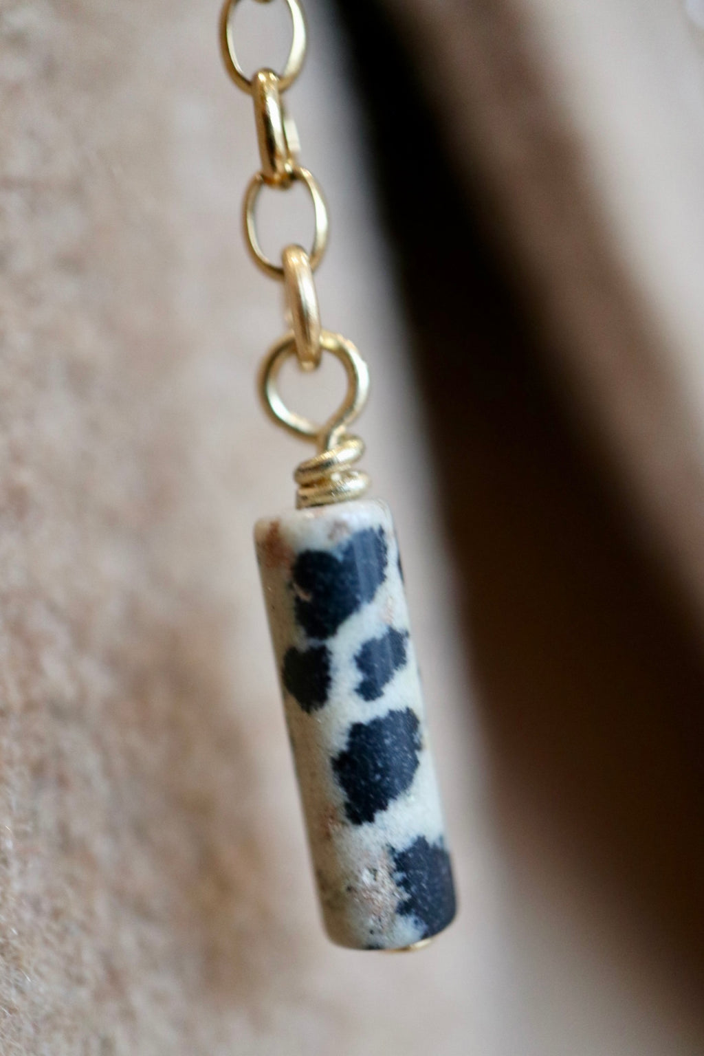 Macro close-up of the Perrin brooch by Auréad Designs showing the natural black and white spotted pattern of the Dalmatian jasper cylinder bead suspended from a gold stainless steel rolo chain
