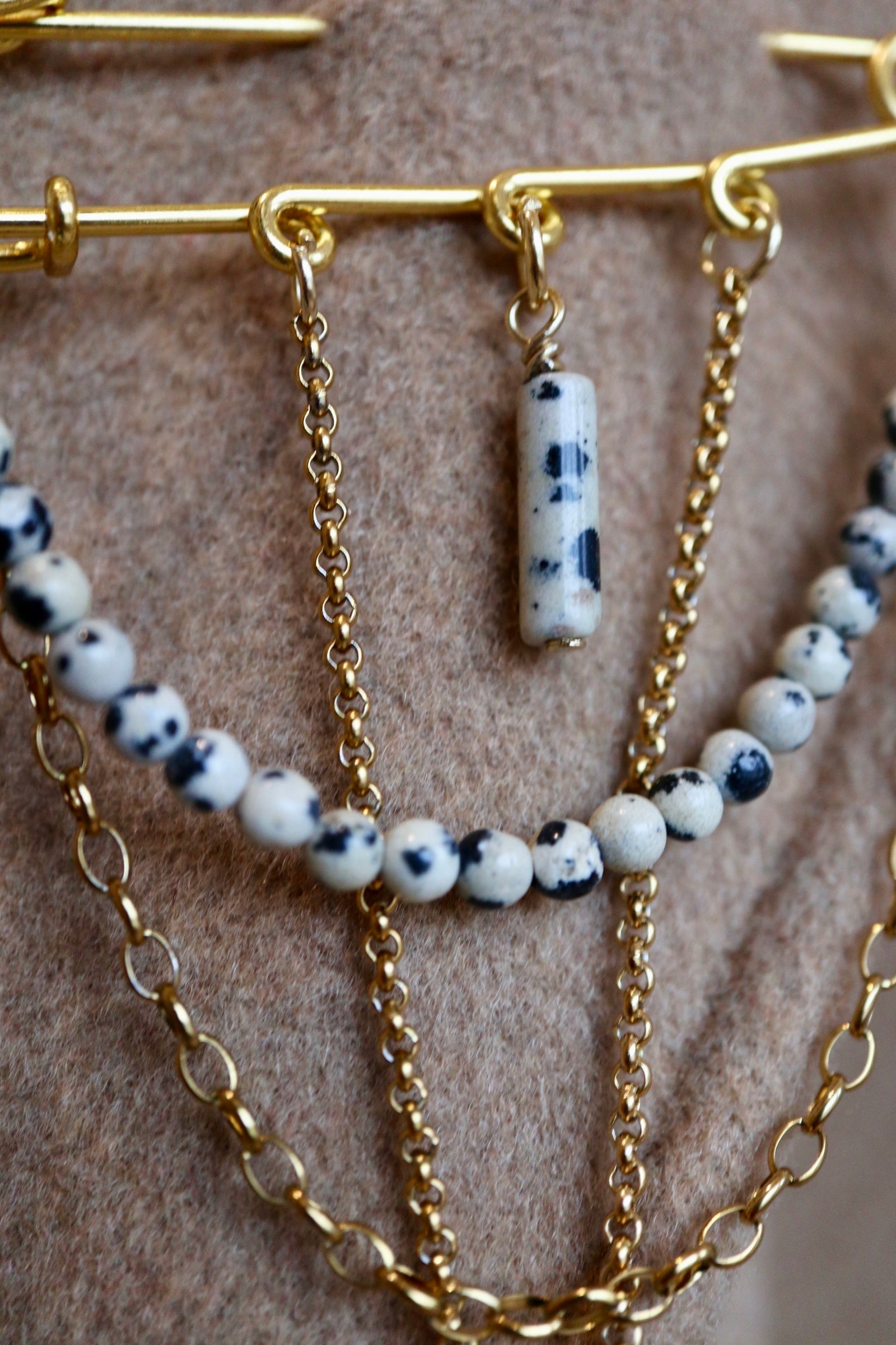 Close-up of the Perrin brooch showing the speckled pattern of Dalmatian jasper beads alongside layered gold stainless steel rolo and cable chains