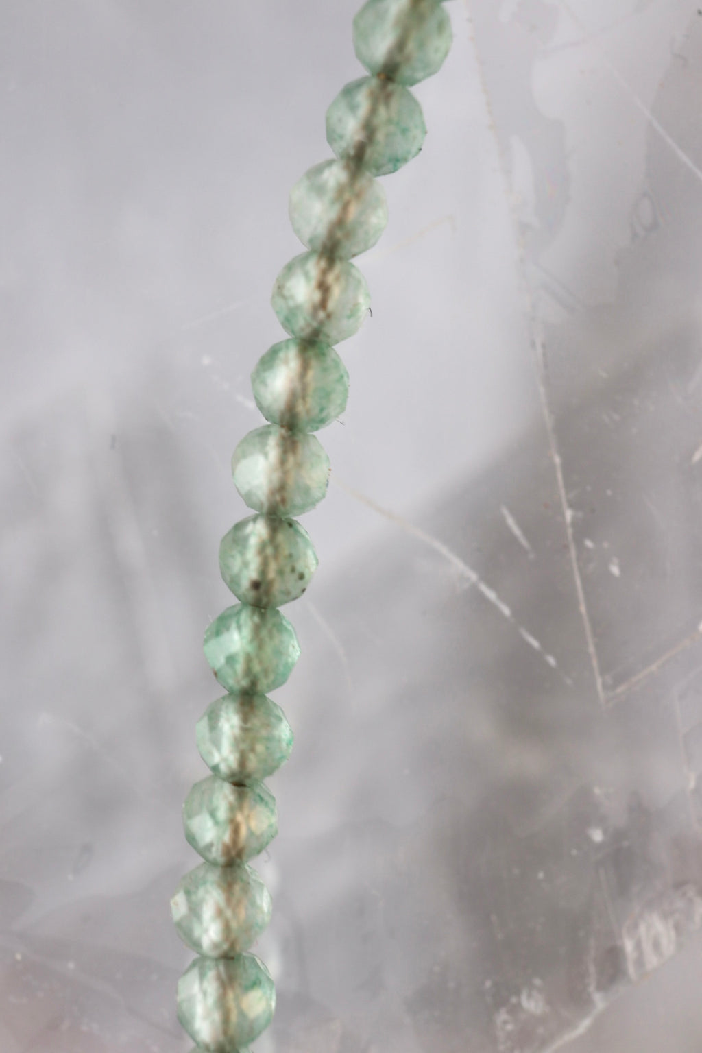 Macro detail of 2mm faceted green aventurine beads from the Auréad Designs Primelle necklace against a selenite slab background, showing natural variation in color and translucency