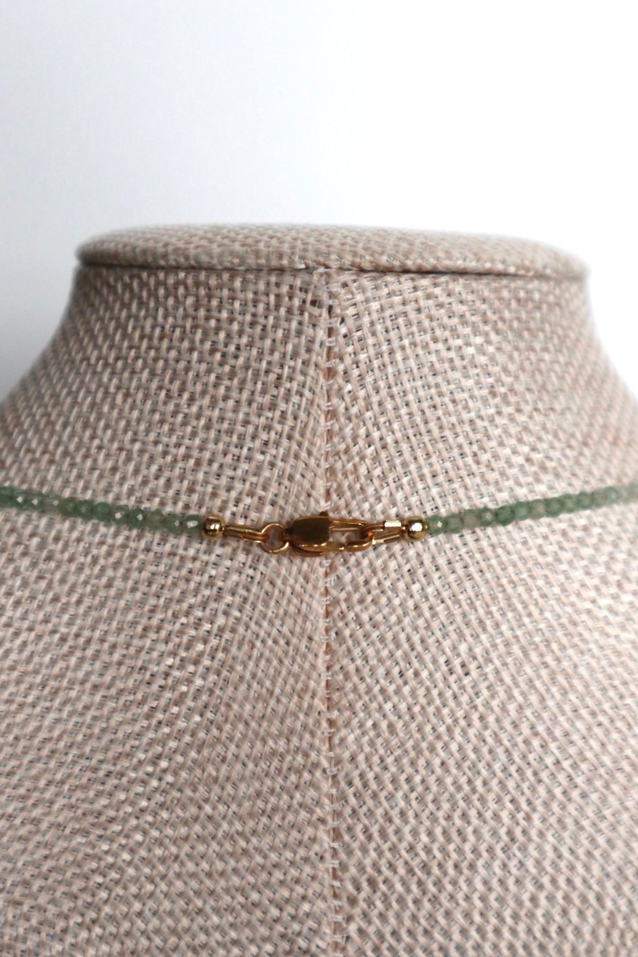 Auréad Designs Primelle necklace back clasp detail showing IP gold stainless steel lobster claw clasp with faceted green aventurine beads on a linen bust form