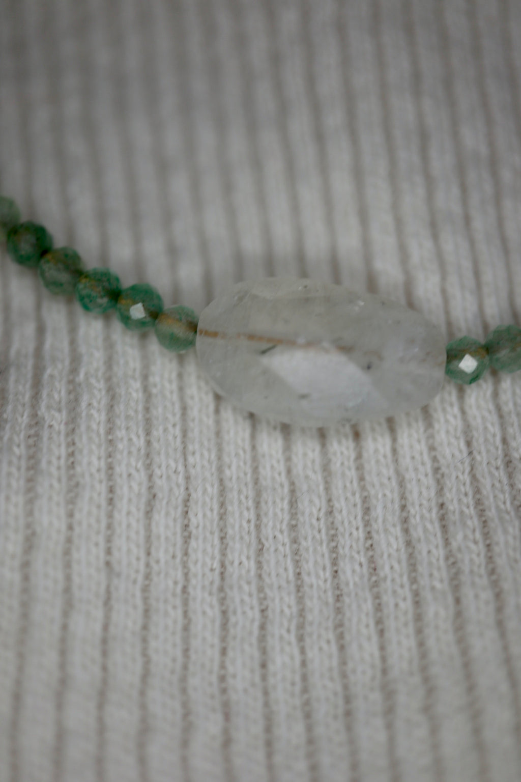 Close-up of the faceted moonstone focal bead at center of the Auréad Designs Primelle necklace resting on a cream ribbed knit fabric