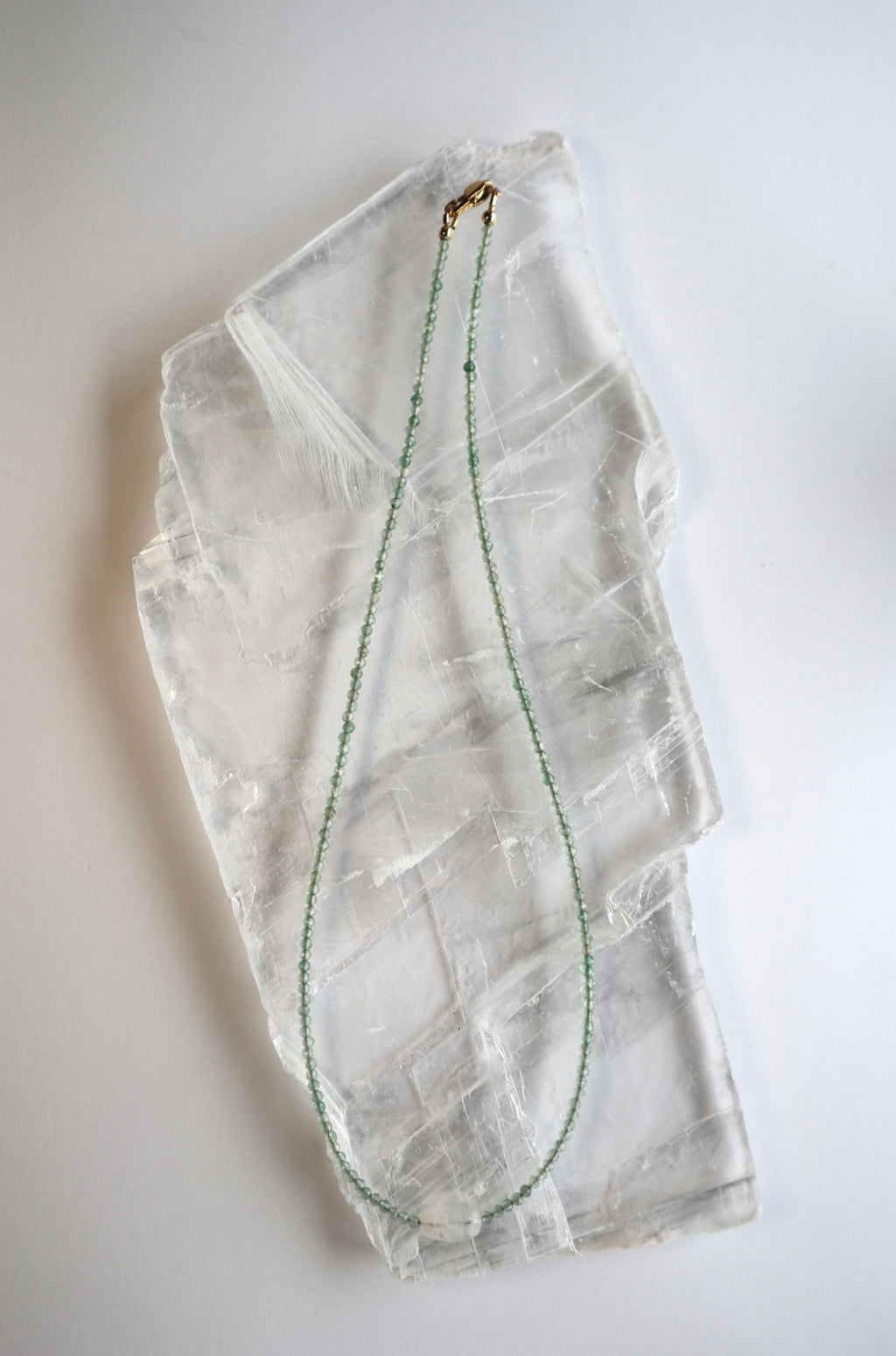 Auréad Designs Primelle necklace laid out in full on a white selenite slab with gold lobster clasp visible at top