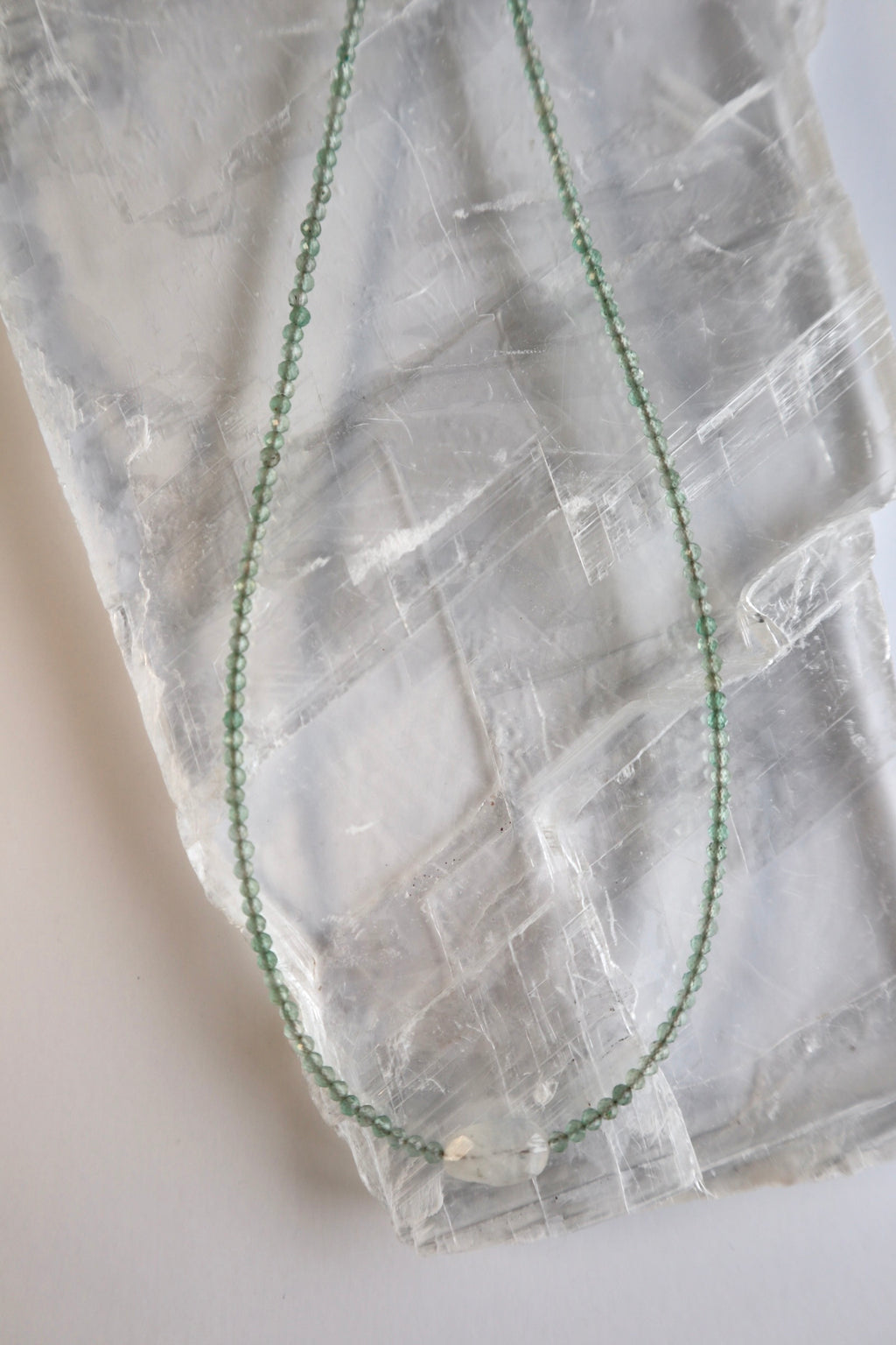 Auréad Designs Primelle necklace displayed in a loop on a white selenite slab showing the full continuous strand of faceted green aventurine beads and moonstone focal
