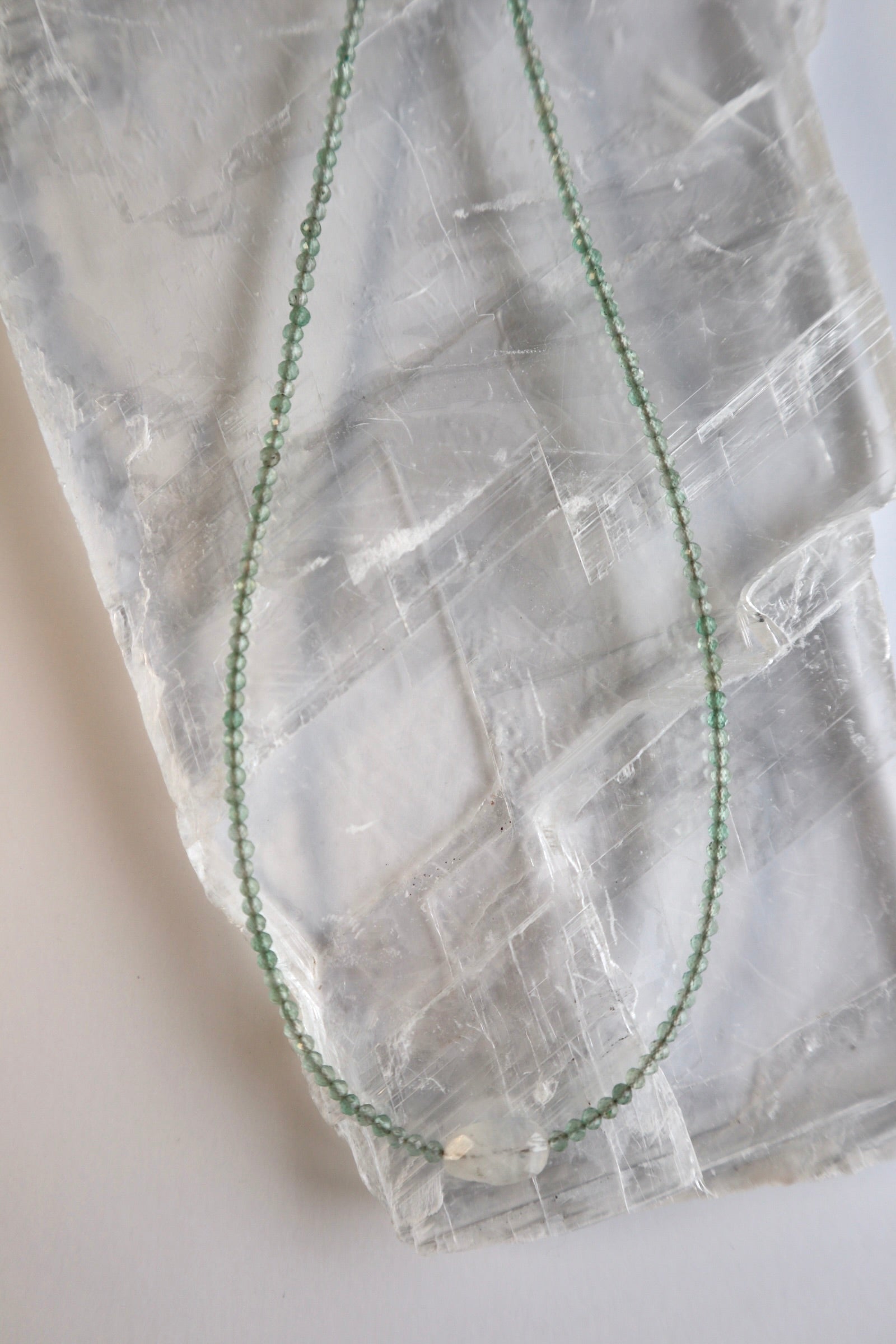 Auréad Designs Primelle necklace displayed in a loop on a white selenite slab showing the full continuous strand of faceted green aventurine beads and moonstone focal