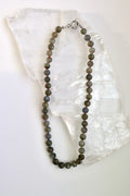 Prism necklace by Auréad Designs, featuring round labradorite gemstone beads on a multicolor ombré silk cord with a stainless steel clasp, laid flat on a white selenite slab