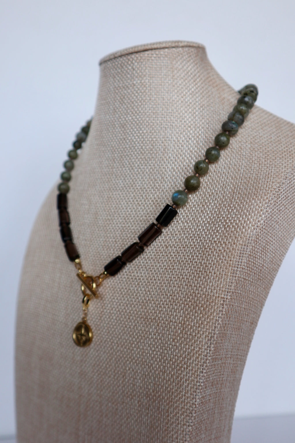 Ridge necklace by Auréad Designs on a linen bust, angled view, with the gold compass charm pendant hanging at center