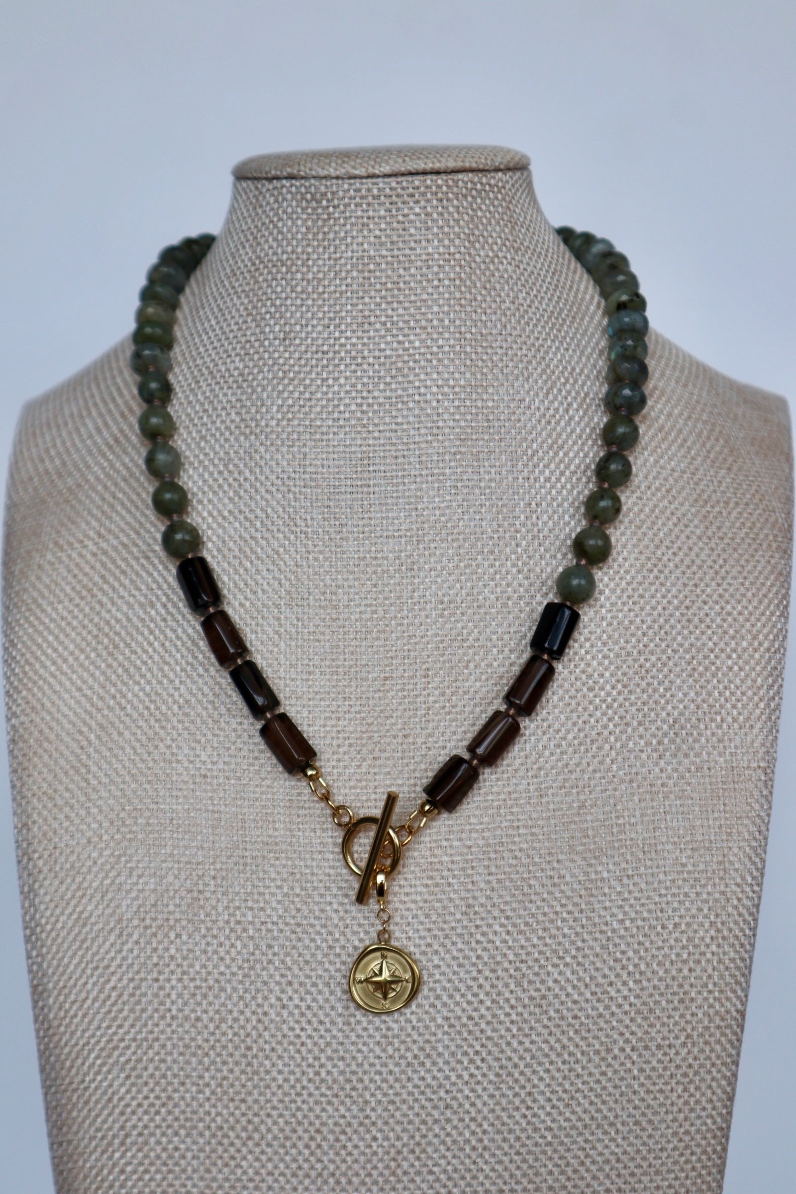 Ridge necklace by Auréad Designs on a linen bust, angled view, with the gold compass charm pendant hanging at center