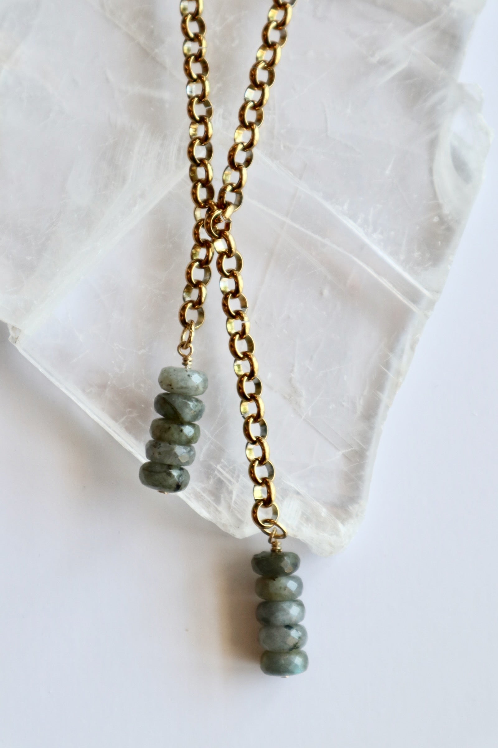 Auréad Designs Rochelle gold rolo chain lariat necklace with two stacked labradorite faceted rondelle drops, flat lay on white selenite slab.