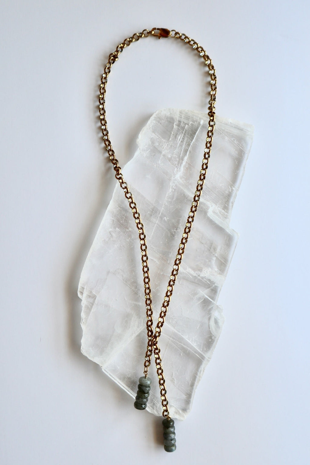 Auréad Designs Rochelle gold rolo chain lariat necklace with labradorite rondelle drop pendants, overhead flat lay on white selenite slab showing full 21-inch length.