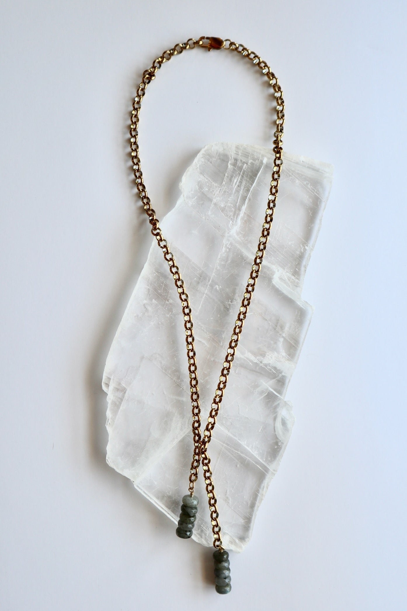 Auréad Designs Rochelle gold rolo chain lariat necklace with labradorite rondelle drop pendants, overhead flat lay on white selenite slab showing full 21-inch length.