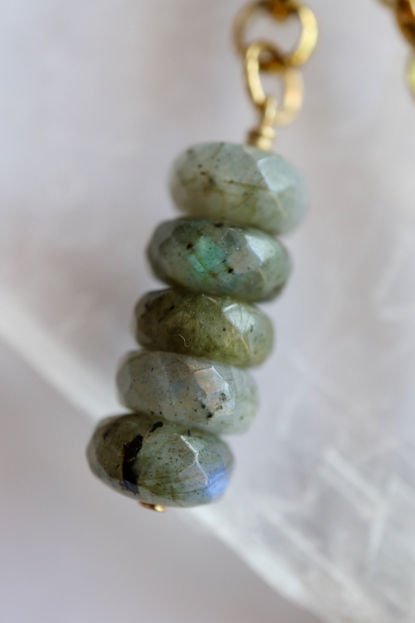 Macro detail of Auréad Designs Rochelle labradorite faceted rondelle drop pendant showing blue and green labradorescence on white selenite slab.