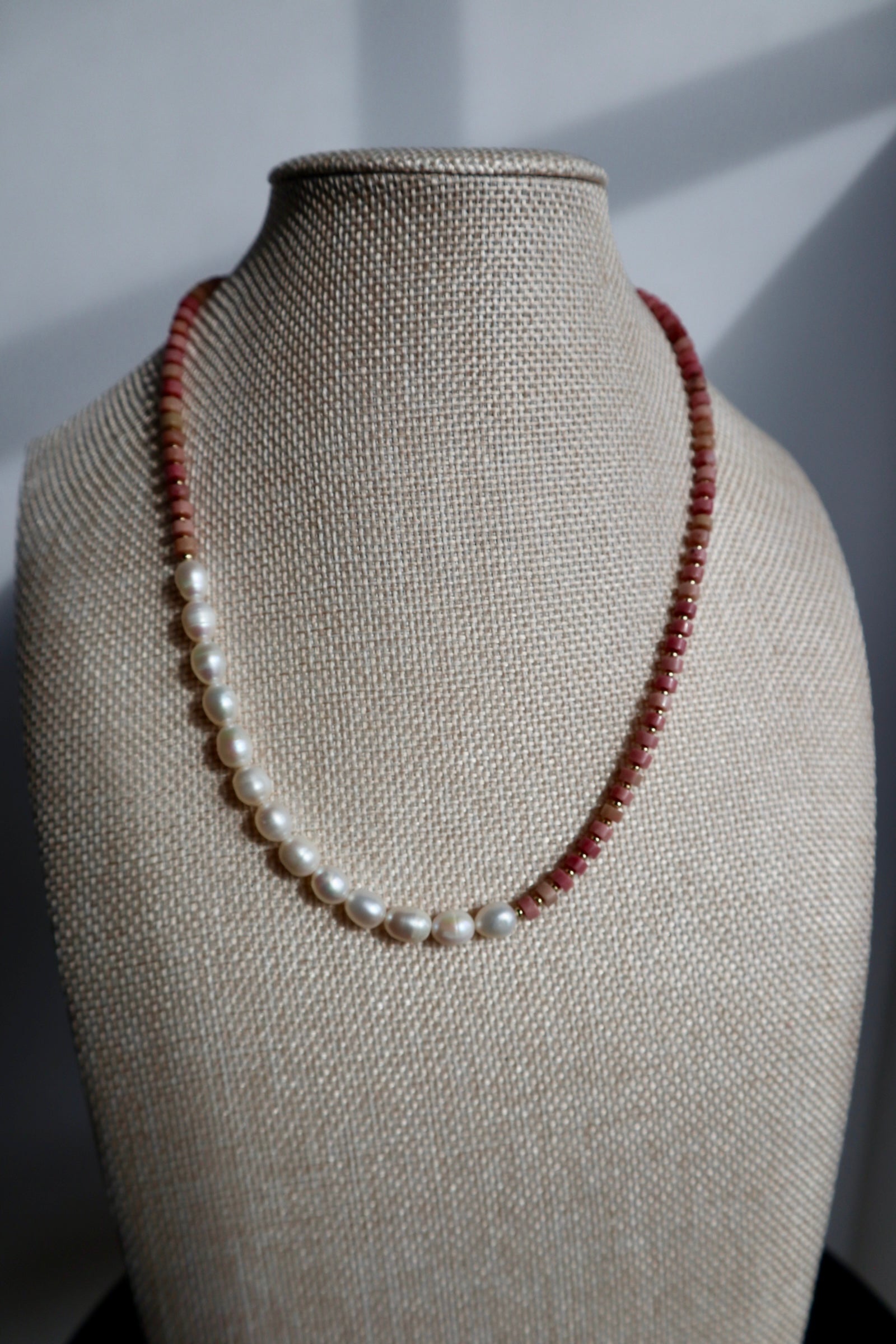 Rosera necklace by Auréad Designs displayed on a linen bust form, showing the full strand with the asymmetrical freshwater pearl section transitioning into rhodonite heishi beads