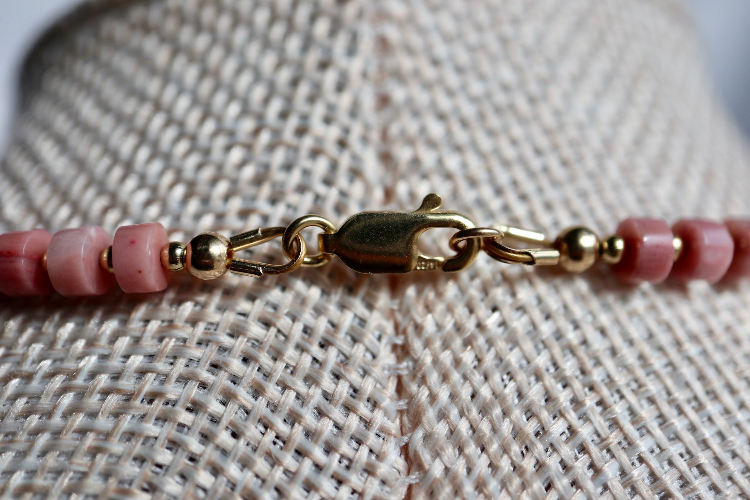 Detail shot of the Rosera necklace showing the 14k gold-filled lobster clasp and the contrast between rhodonite heishi beads, freshwater pearls, and gold spacer beads