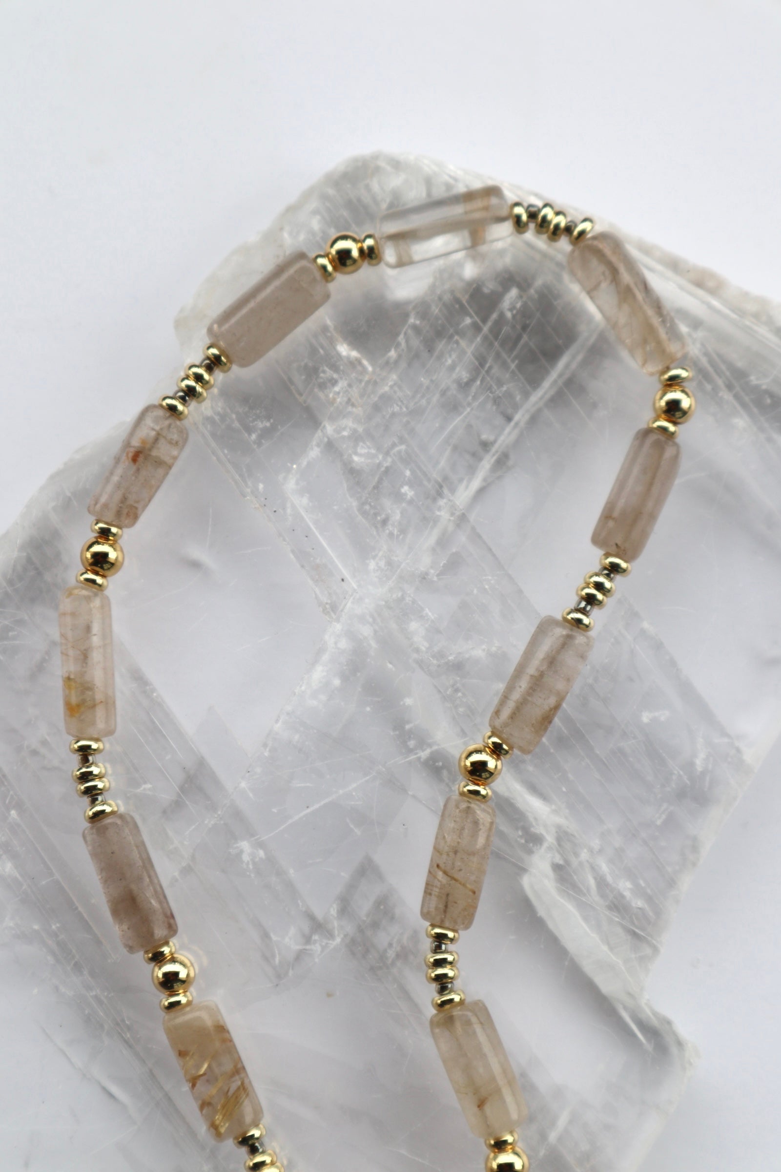 Close-up of the Rutila necklace showing the golden inclusions within rutilated quartz cylinder beads alongside galvanized gold spacers and dark gray glass seed beads