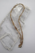 Rutila necklace by Auréad Designs, featuring rutilated quartz cylinder beads, galvanized gold spacer beads, and dark gray glass seed beads with a gold-filled toggle clasp, laid flat on a white selenite slab