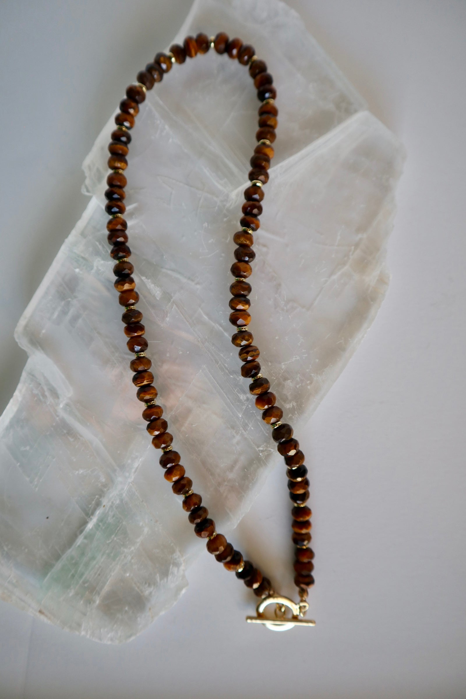 Sable necklace by Auréad Designs, featuring tiger eye gemstone beads and gold-filled spacer beads with a gold-filled toggle clasp, laid flat on a white selenite slab