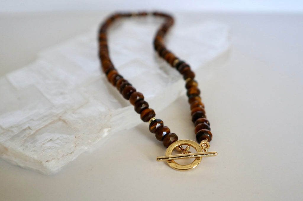 Sable necklace by Auréad Designs laid flat on a white selenite slab, with the gold-filled toggle clasp in the foreground and the full tiger eye bead strand extending behind it