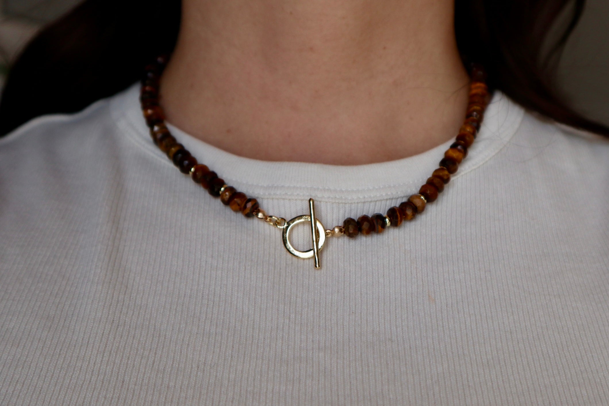 Sable necklace by Auréad Designs worn with the gold-filled toggle clasp centered at the front, styled with a white ribbed top, showing the clasp as a focal detail against tiger eye beads