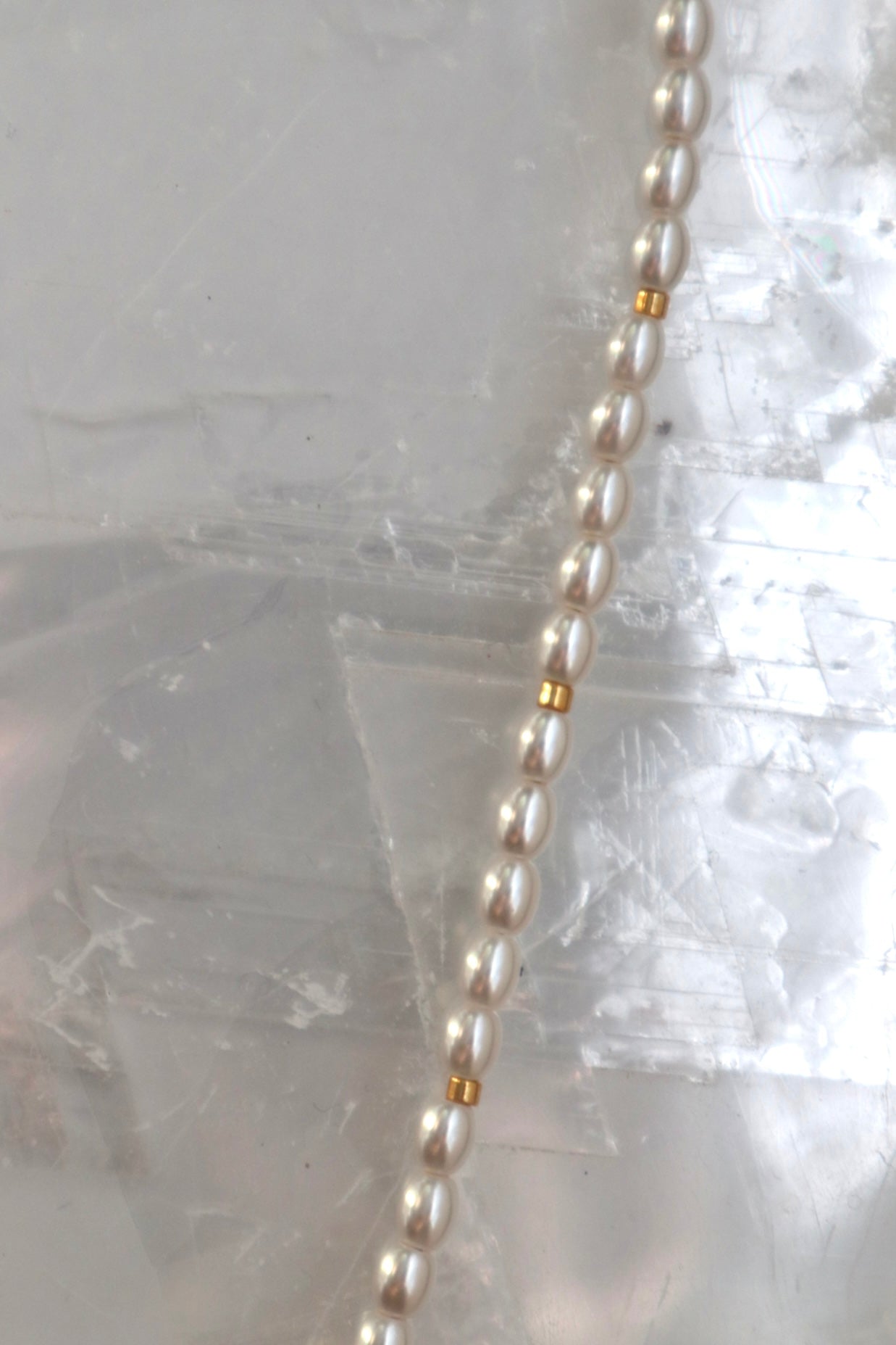 Close-up of the Selene necklace by Auréad Designs showing the glass pearl strand and galvanized gold spacer beads resting on a white selenite slab