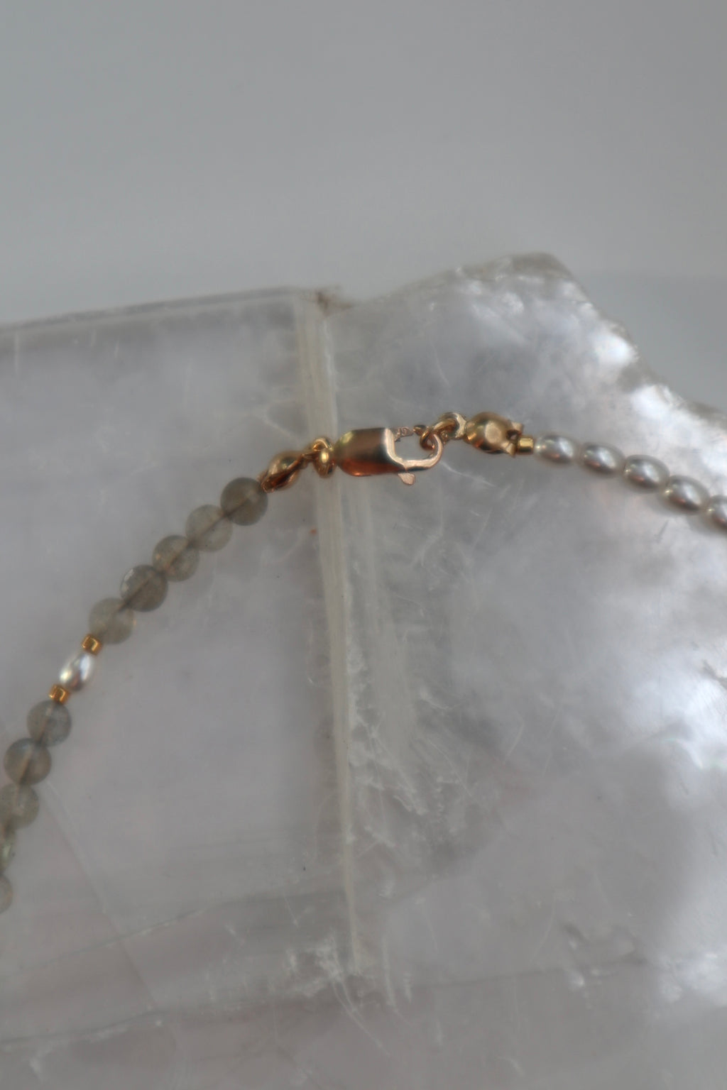 Close-up of the Selene necklace showing the 14k gold-filled lobster clasp and faceted labradorite beads resting on a white selenite slab