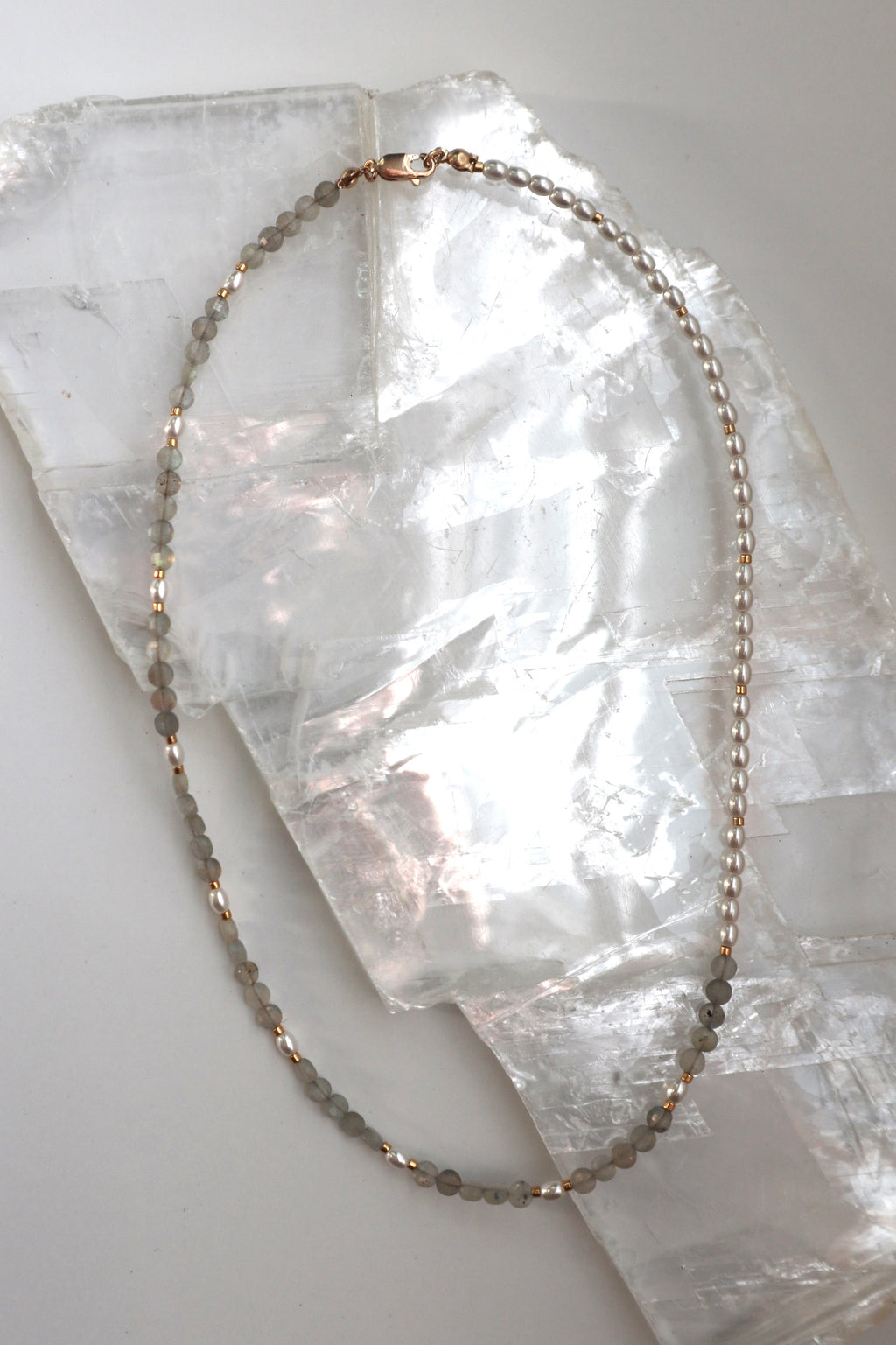 Selene necklace by Auréad Designs, featuring faceted labradorite beads and glass pearls with a 14k gold-filled clasp, laid flat on a white selenite slab