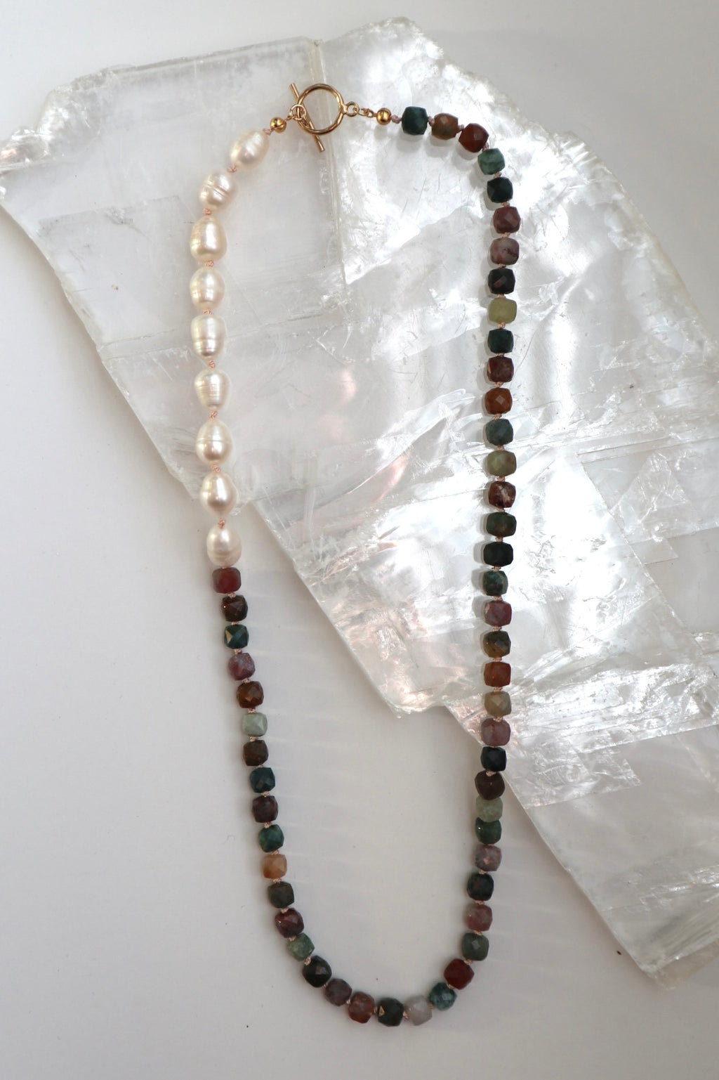 Siena necklace by Auréad Designs, featuring Indian agate gemstone beads and freshwater pearls on a silk-knotted strand with a 14k gold-filled toggle clasp, laid flat on a white selenite slab