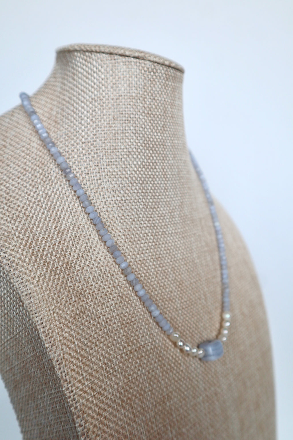 Sky necklace by Auréad Designs on a linen bust, angled view, showing the delicate blue lace agate rondelles and freshwater pearl accents leading to the rectangular focal bead